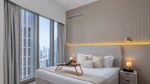 A modern hotel room with a large bed, a bedside table with a lamp, a nightstand, and a view of the city through large windows. - Maison Privee Sky-High Elegance w/ Unrivaled Burj Khalifa Views (Dubai)