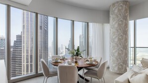 A modern dining area with a round table set for four, large windows offering a city view, and a tall decorative column. - Maison Privee Sky-High Elegance w/ Unrivaled Burj Khalifa Views (Dubai)