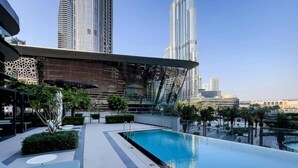 A rooftop pool with lounge chairs and a modern building with a unique facade in the background. - Maison Privee Sky-High Elegance w/ Unrivaled Burj Khalifa Views (Dubai)