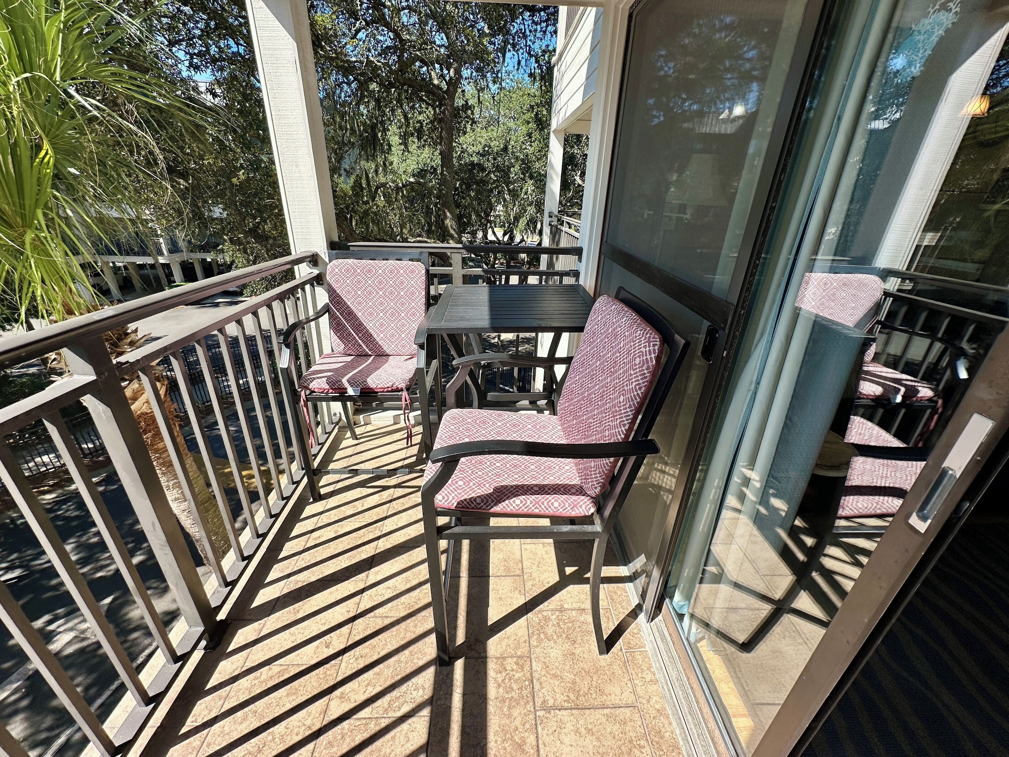 Ein Balkon mit Tisch und Stühlen, einer Glastür und Blick auf Bäume sowie ein Gebäude.