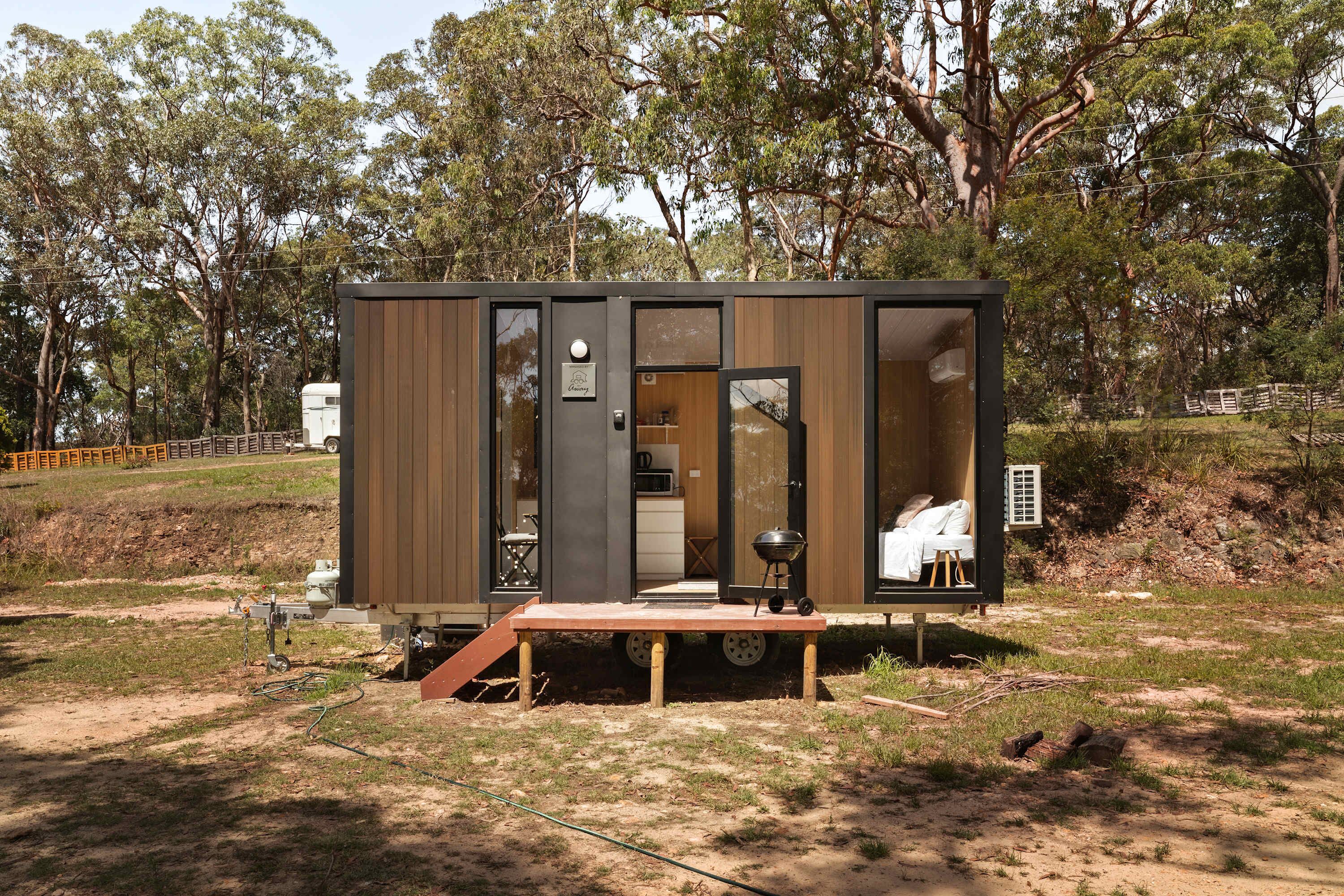 Una cabaña pequeña y moderna con entrada por puerta corrediza, un pequeño porche y una cocina visible con una parrilla.