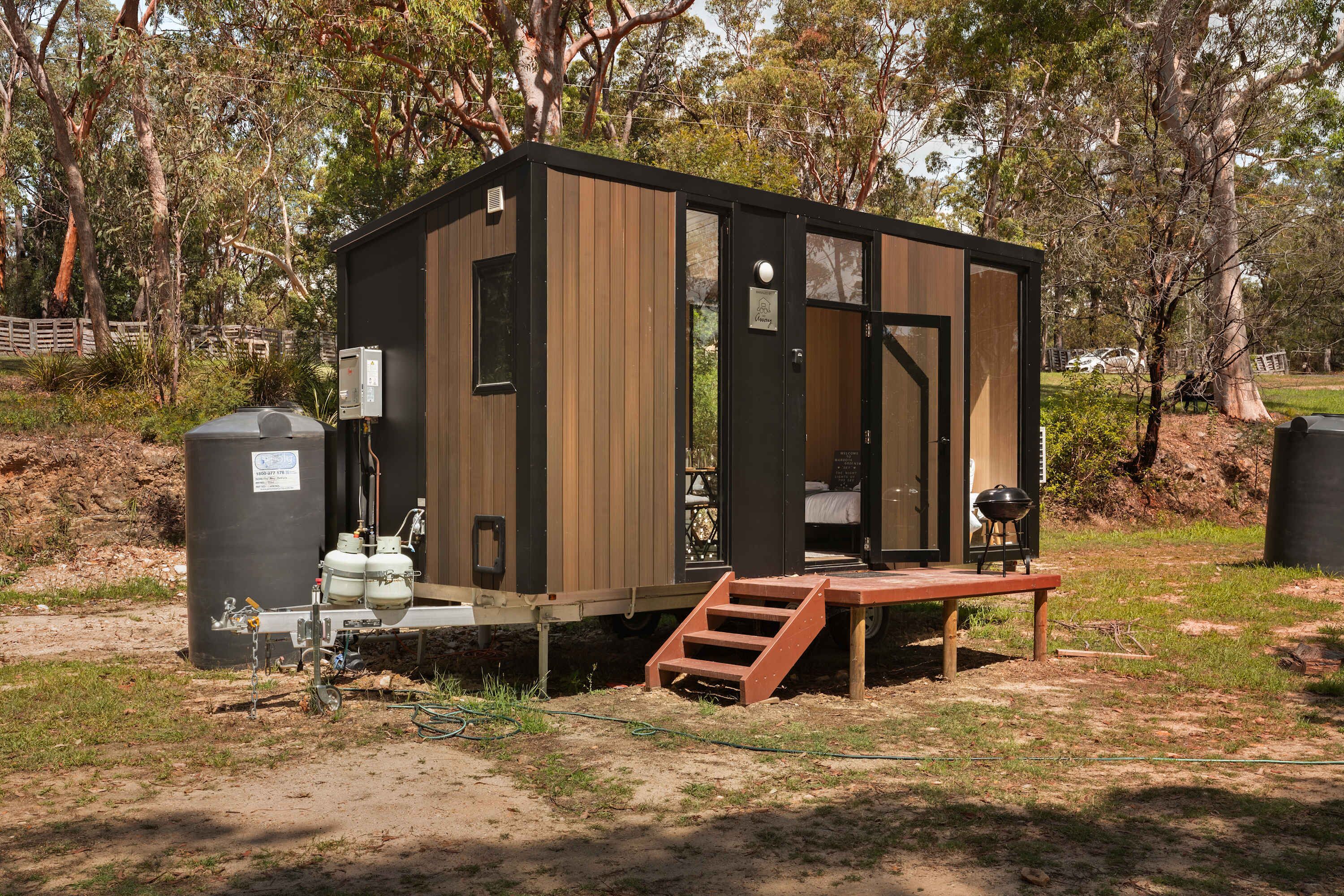 A small, wooden cabin with a front door, a small porch, and a grill outside.