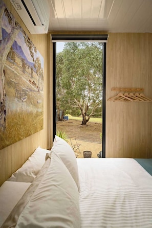 Un dormitorio con una cama grande, un cuadro en la pared, una puerta de madera y vistas a un árbol y un espacio exterior.