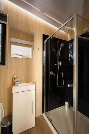 A modern bathroom with a glass-enclosed shower, a white sink, and a wooden vanity. - Bush Serenity by the Sea by Tiny Away (Bolwarra)