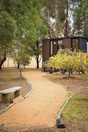A small, modern cabin with a gravel path leading to it, surrounded by trees and a garden area. - Bush Serenity by the Sea by Tiny Away (Bolwarra)