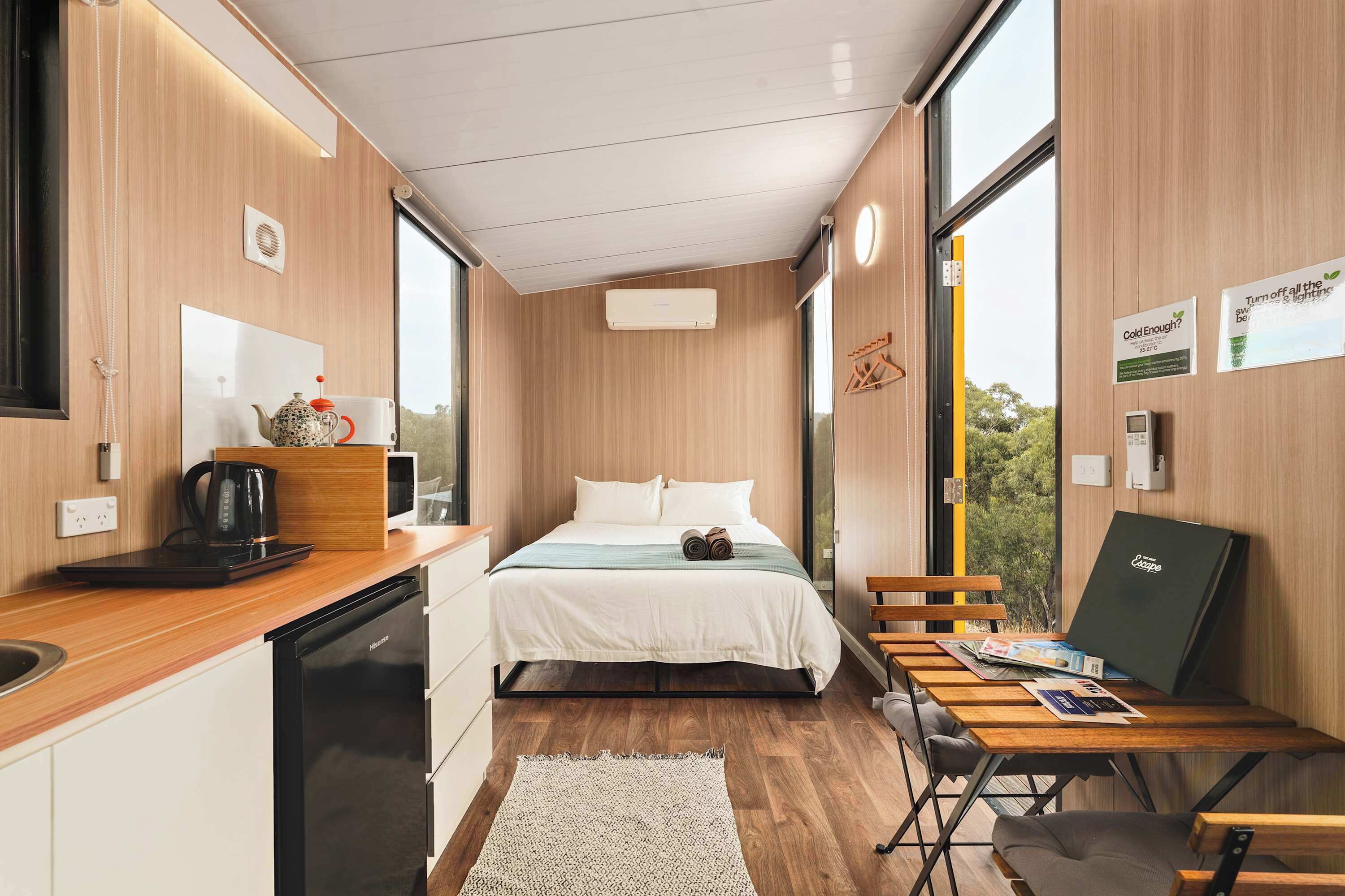 A modern room with a bed, a desk, a chair, a coffee maker, and a window.