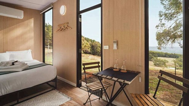 A modern bedroom with a large bed, a wooden table with two wine glasses, and a view of the outdoors. - Dreamy 1 by Tiny Away (Red Hill)
