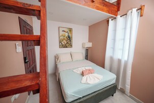 Una cama bien hecha con una colcha azul claro y una almohada blanca, un cuadro de un pájaro en la pared y un marco de puerta de madera.
