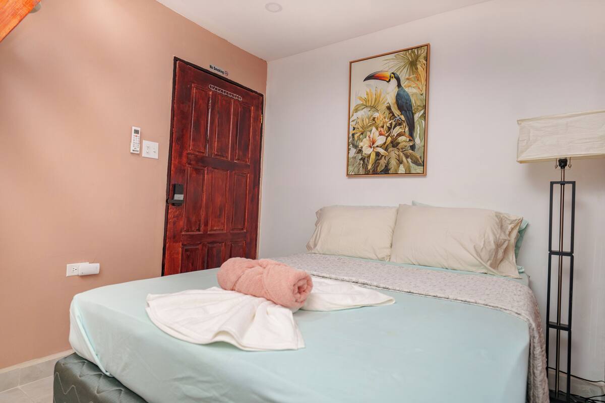 A bedroom with a bed, a door, a painting, and a floor lamp.
