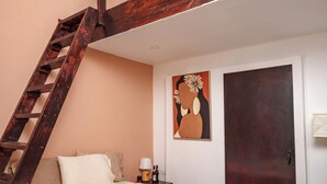 Ein Schlafzimmer mit Bett, Nachttisch, Lampe, einem Gemälde und einer Holztreppe.