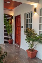 Un pasillo con techo de madera, una puerta roja y plantas en macetas.