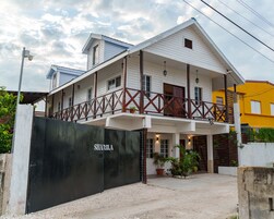 Un edificio de dos pisos con un balcón, una entrada con portón y un letrero que dice "SHARILA".