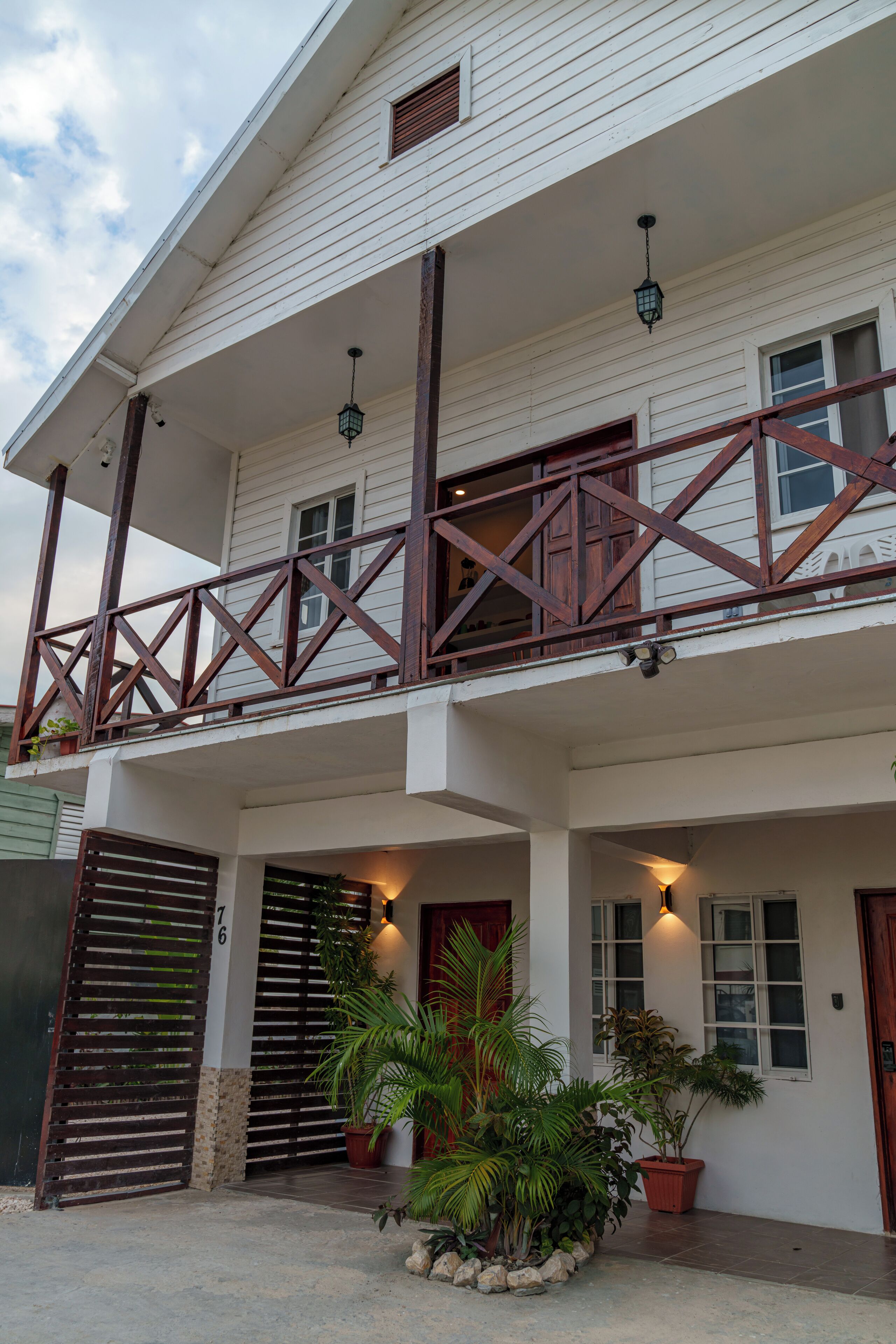 A two-story building with a balcony, potted plants, and a gated entrance.