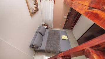 Un dormitorio con una cama, una mesita de noche, una lámpara y una ventana con cortina.