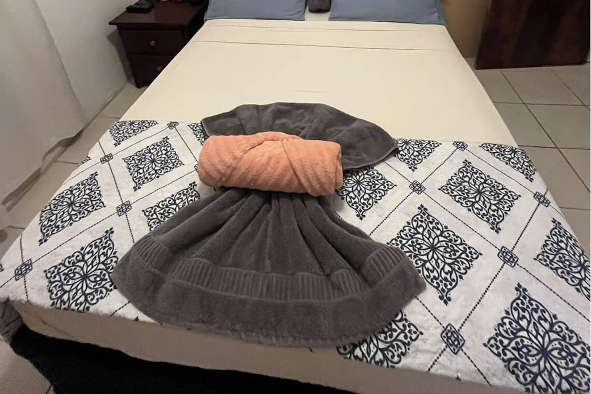 A hotel room with a bed, a painting of a rocky landscape, a nightstand, and a door.