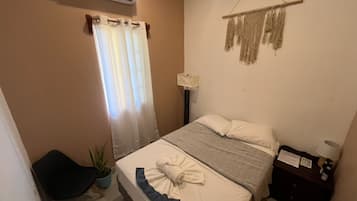 Un dormitori amb un llit, una taula de nit, una làmpada, una planta i aire condicionat fixat a la paret.