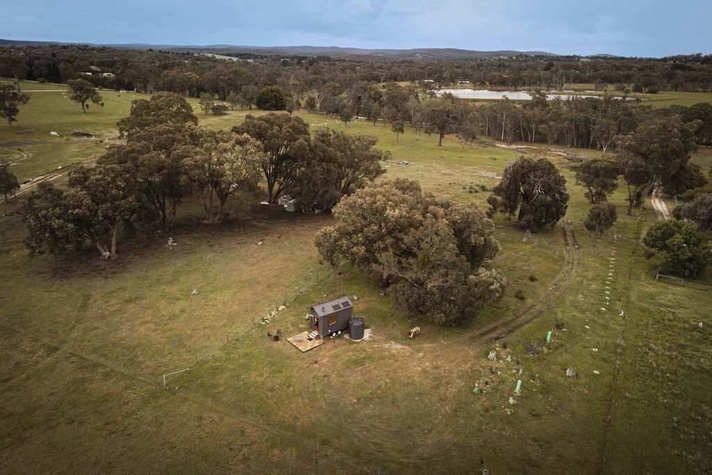 An aerial view of a rural property with a small cabin, open fields, and scattered trees.