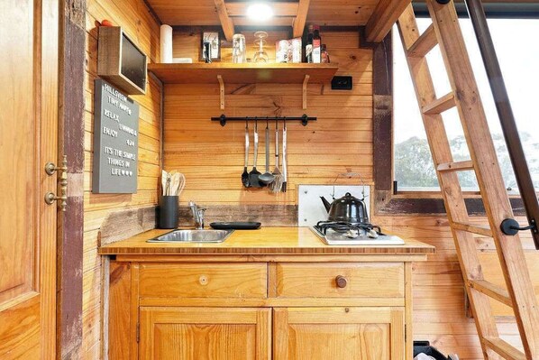 A wooden cabin kitchen with a wooden countertop, a stove, hanging utensils, and a chalkboard with a message.