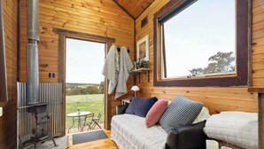 Interior acogedor de una cabaña con cama, sofá, una mesita con velas y una estufa de leña.