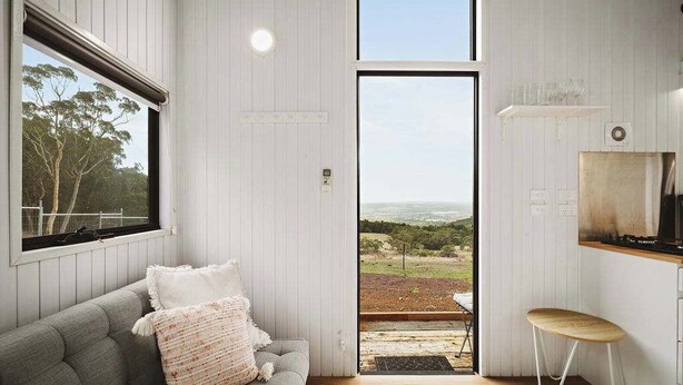 Un interior moderno con un sofá gris, una mesa de comedor de madera y un amplio ventanal con vistas al exterior.
