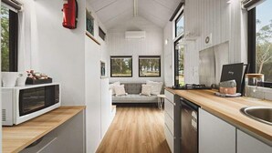 Cocina americana y sala de estar integradas, con piso de madera, armarios blancos y ventanas amplias.