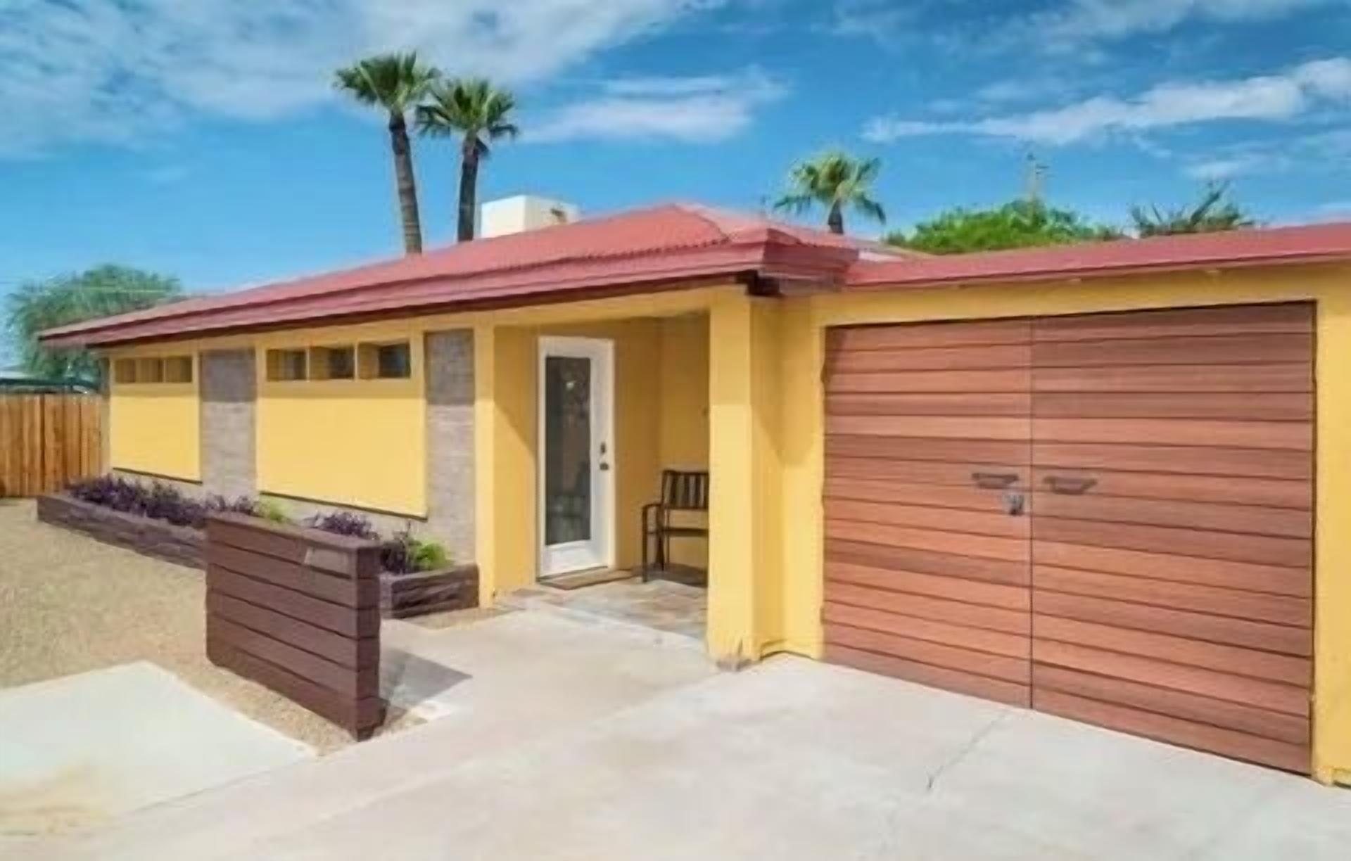 Una casa de un piso con tejado rojo, paredes amarillas y puerta de garaje marrón.