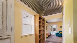 Un couloir avec une bibliothèque en bois, une porte blanche et un canapé bleu à l’arrière-plan.
