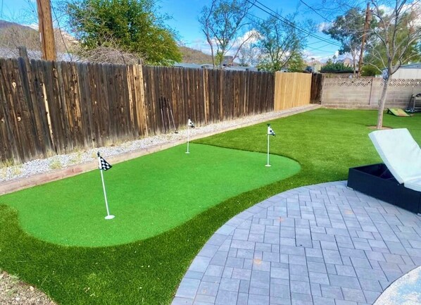 A backyard with artificial grass, a brick patio, and a wooden fence.