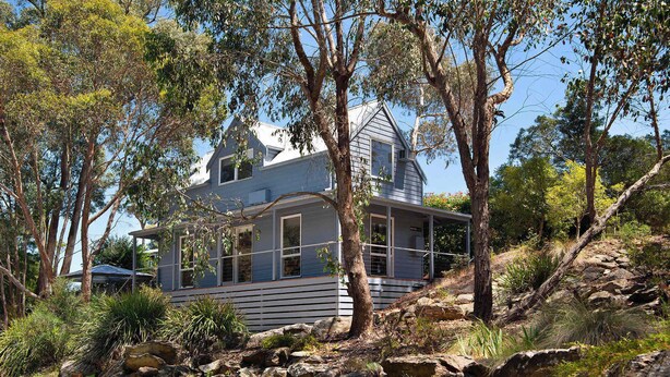 A house with a gabled roof, large windows, and a covered porch, surrounded by trees and rocky terrain. - Kingfisher Loft – 2BR Spa Bath Retreat near Daylesford & Hepburn Springs (Daylesford)