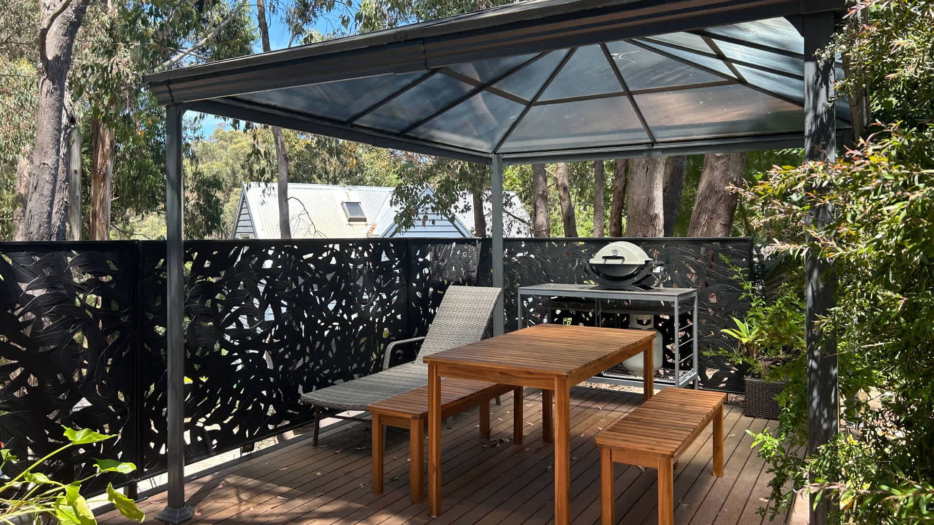 Un patio techado al aire libre con una mesa y sillas de madera, una parrilla y un cerramiento de vidrio.