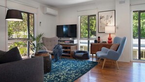 A living room with a TV, seating, a rug, and large windows. - Kingfisher Loft – 2BR Spa Bath Retreat near Daylesford & Hepburn Springs (Daylesford)