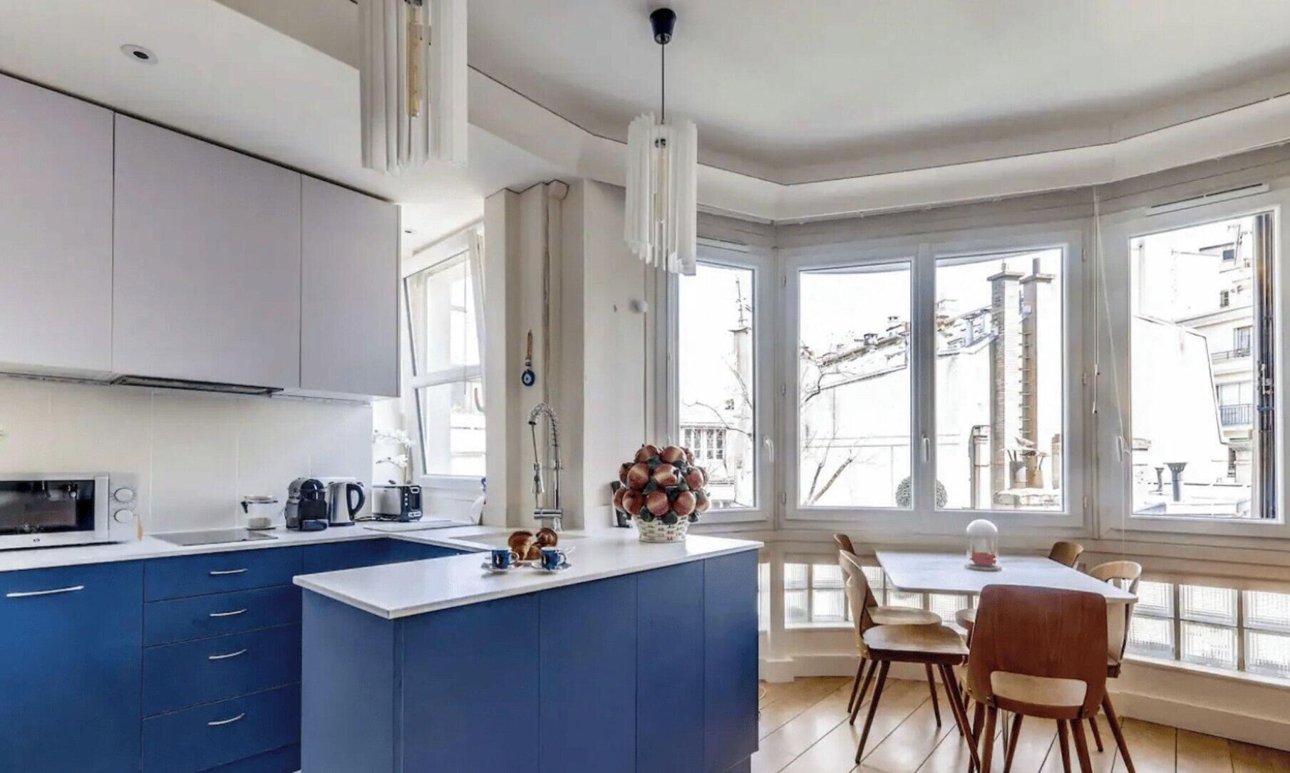 Une cuisine moderne avec un îlot central bleu, des armoires blanches et un coin repas comprenant une table et des chaises.