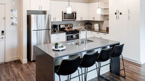 Une cuisine moderne dotée d’appareils électroménagers en acier inoxydable, d’un îlot central avec des tabourets de bar et de meubles de rangement blancs.