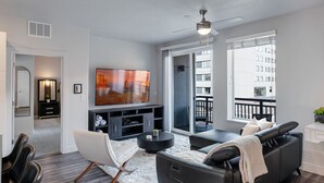 Un salon moderne avec un canapé gris, un fauteuil blanc et un téléviseur à écran plat.