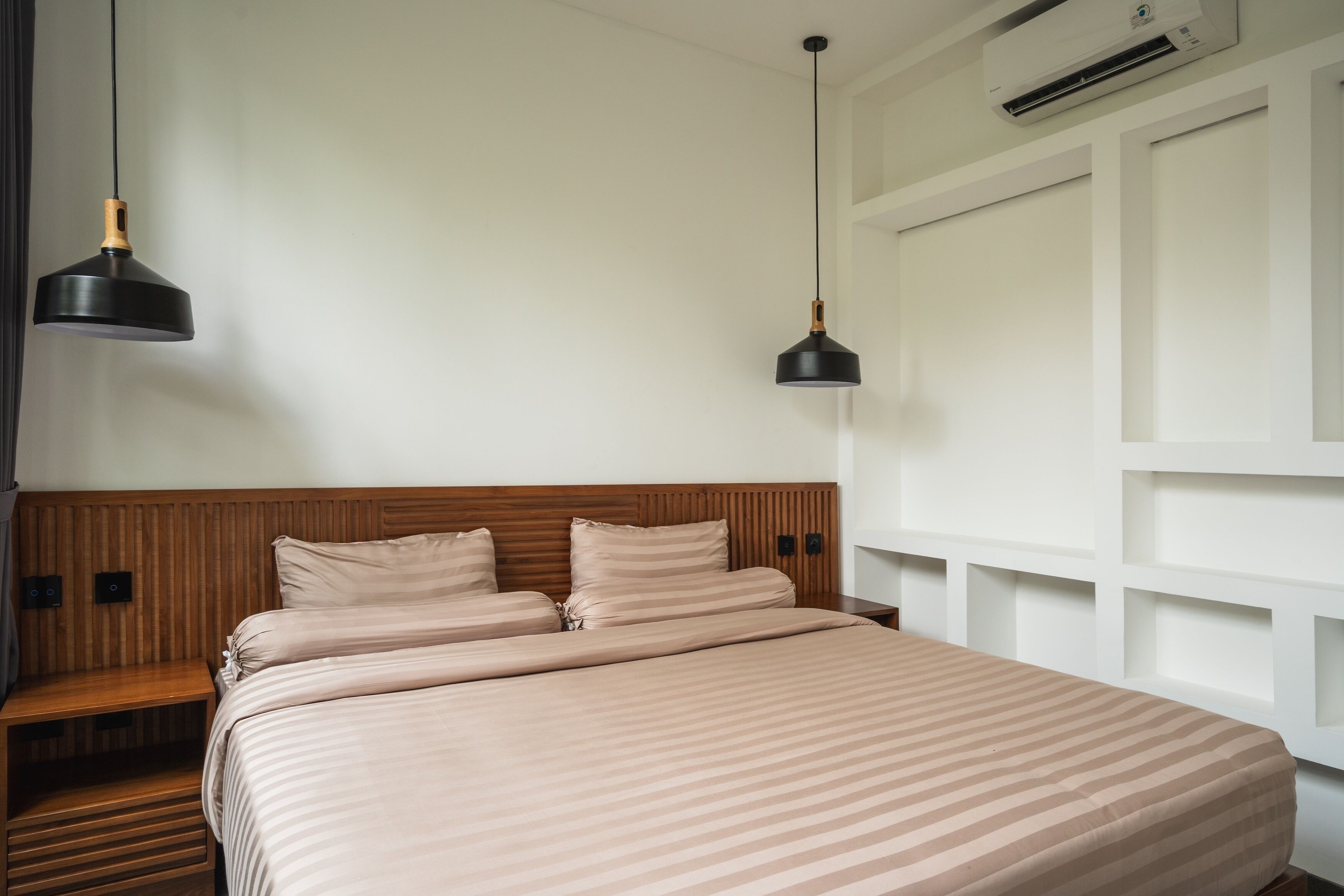Un lit bien fait, avec une couvre-lit à rayures, une tête de lit en bois et deux lampes suspendues.