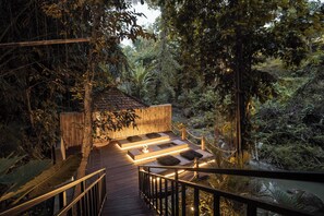 A wooden deck with built-in seating and a fire feature, surrounded by dense tropical vegetation. - Villa Kenji by Alfred in Bali (Canggu)
