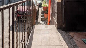 A narrow urban street with buildings on either side, a gated entrance, and parked cars.