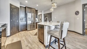 A modern kitchen with stainless steel appliances, a central island with bar stools, and a pendant light fixture.