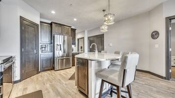 A modern kitchen with stainless steel appliances, a central island with bar stools, and a pendant light fixture.