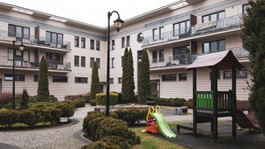 Un patio con un parque infantil, que incluye un tobogán y una estructura de escalada, rodeado de arbustos y árboles bien cuidados.