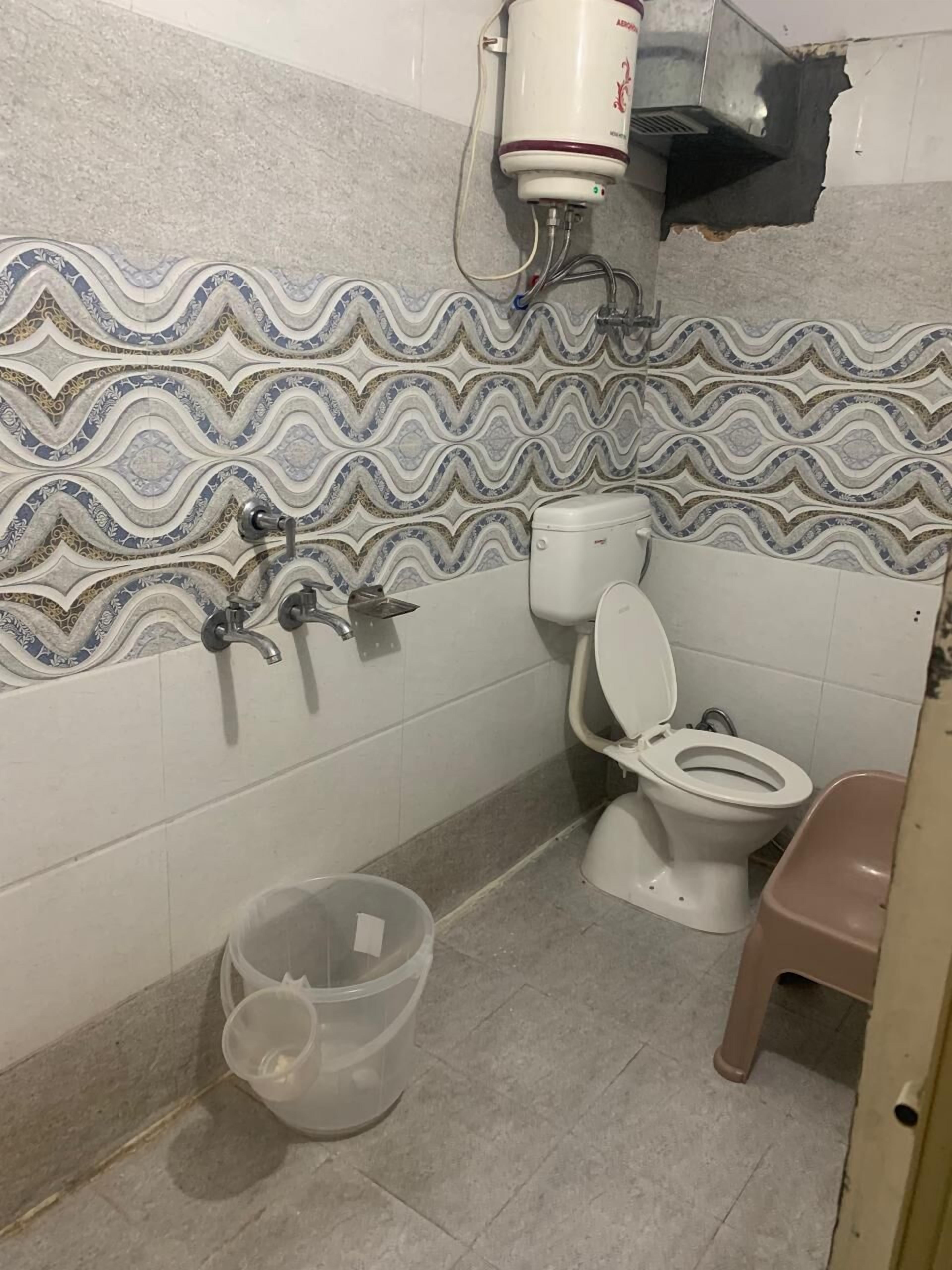 Et badeværelse med et mønstret flisebordsplade, toilet, vask og skraldespand.