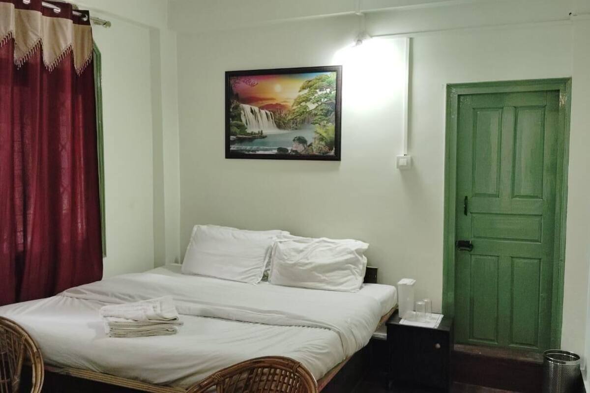 Een kamer met een bed, een stoel, een groene deur en een schilderij aan de muur.