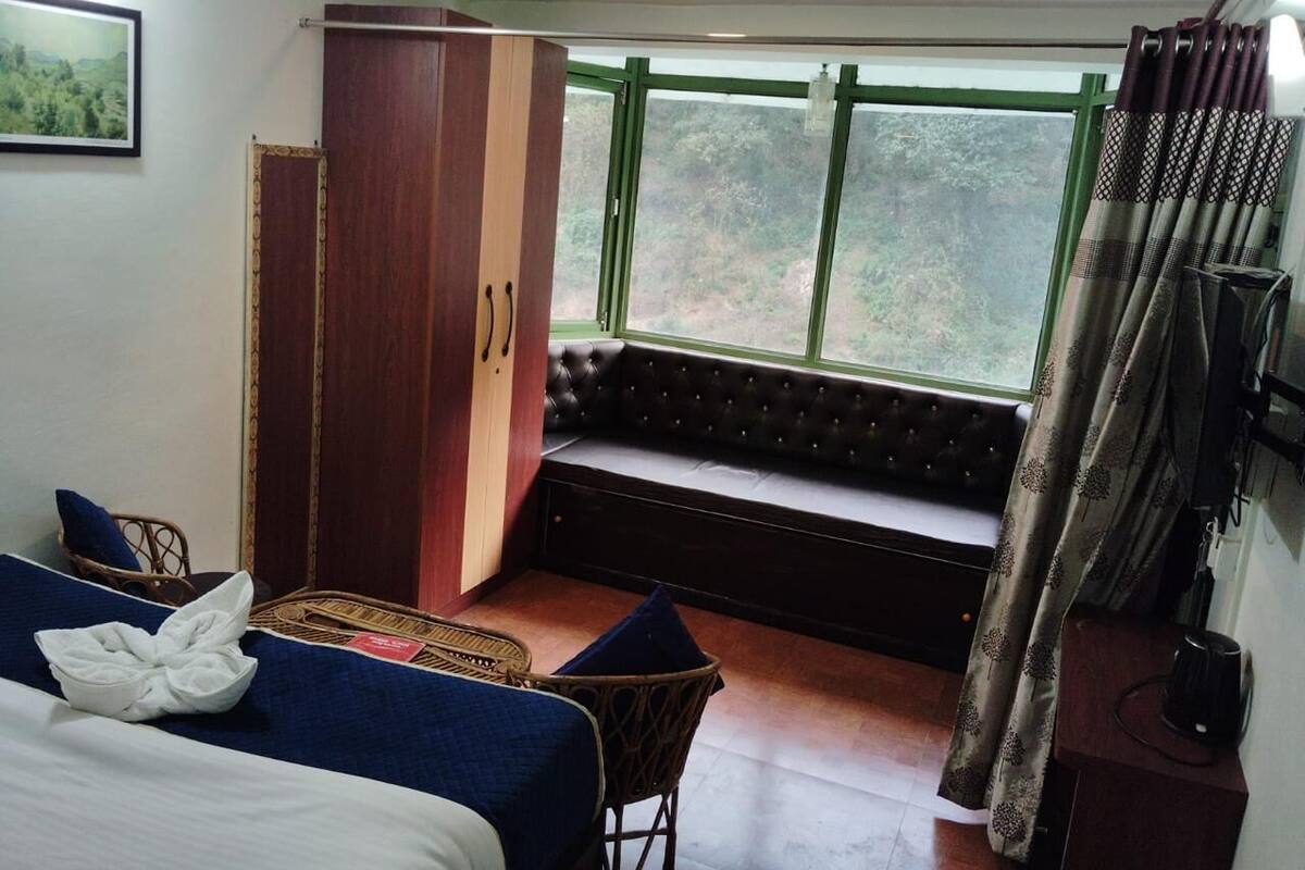 Een kamer met een bed, een bankje bij het raam, een kledingkast en een kleine tafel.
