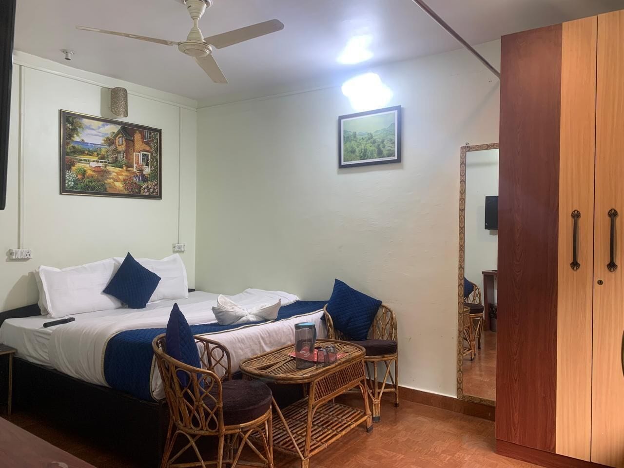 A bedroom with a bed, two chairs, a table, a wardrobe, and two framed pictures on the wall.