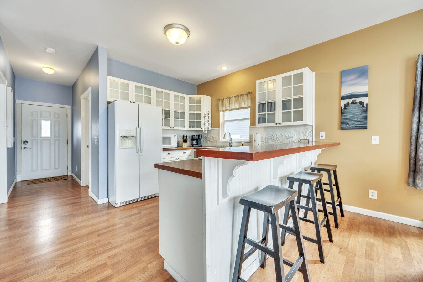 A modern kitchen with white cabinetry, a wooden island with bar stools, and a view of the cityscape through the window.