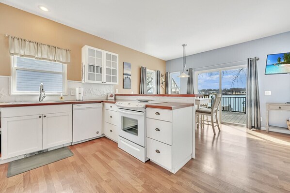 A modern kitchen with white cabinets, a built-in oven, and a dining area with a view of the sea.