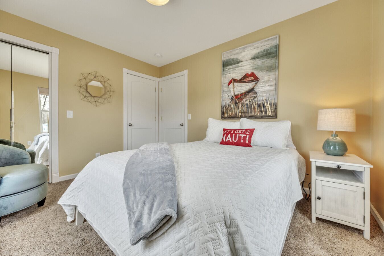A bedroom with a bed, a nightstand, a lamp, a painting, and a door.