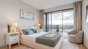 A modern bedroom with a large bed, bedside tables, a chair, and a view of the city through a large window.
