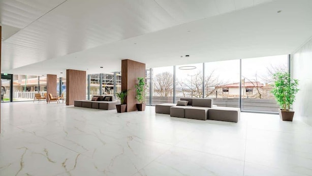 A spacious lobby with a marble floor, seating areas, large windows, and indoor plants.