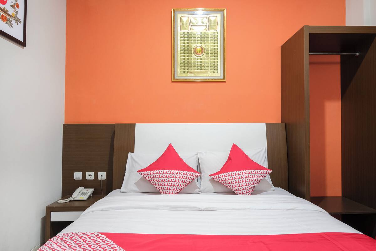 Una habitación de hotel con cama, mesita de noche con teléfono y un cuadro en la pared.